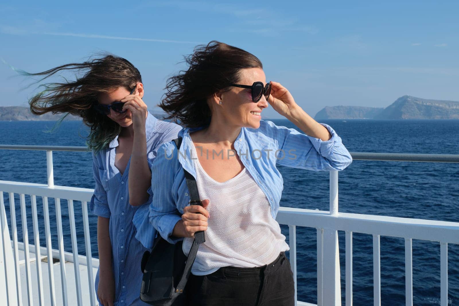 Two women mother and teenage daughter enjoying sea travel on cruise ship, hair flying in the wind