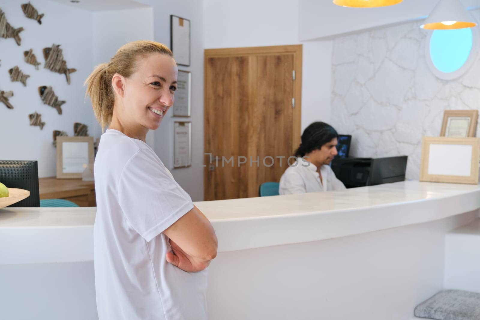 Portrait of spa hotel workers, man and woman near reception, bright interior of resort hotel background