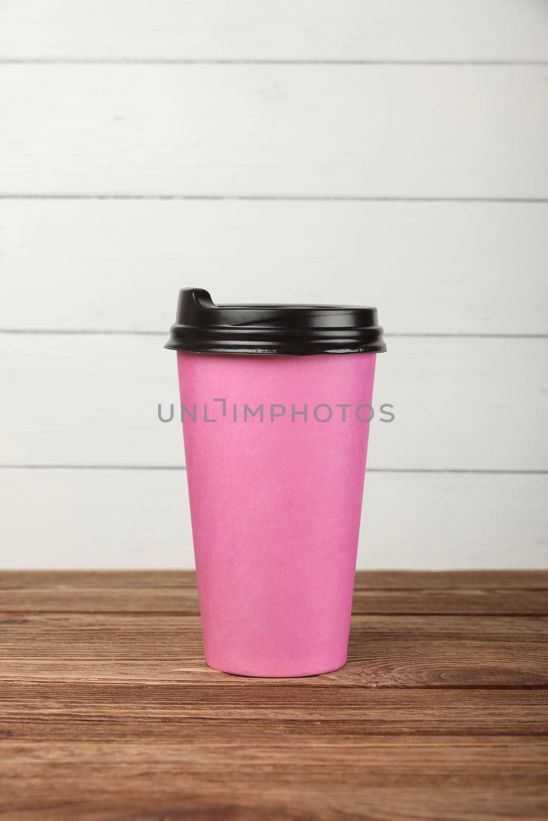 Close up big pink paper coffee cup on brown wooden table over white painted wall at coffee shop retail display