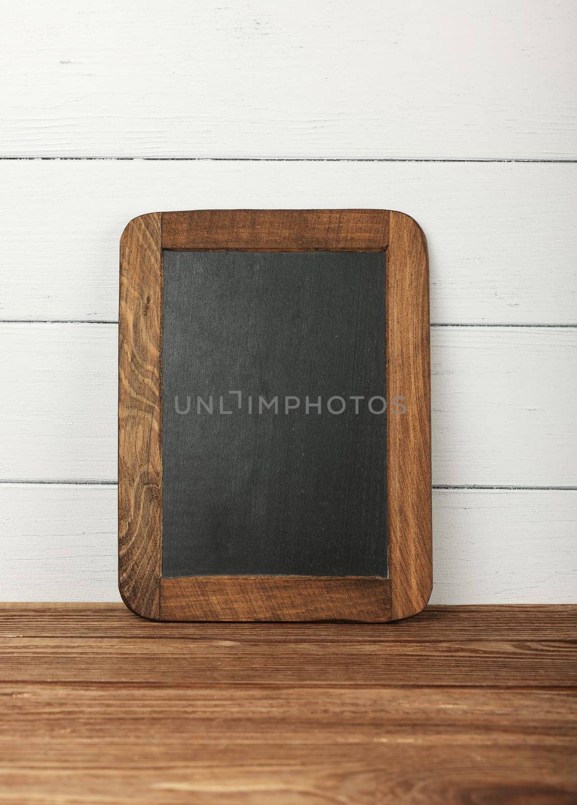 Close up empty blank black slate chalkboard sign over white wooden painted wall on table