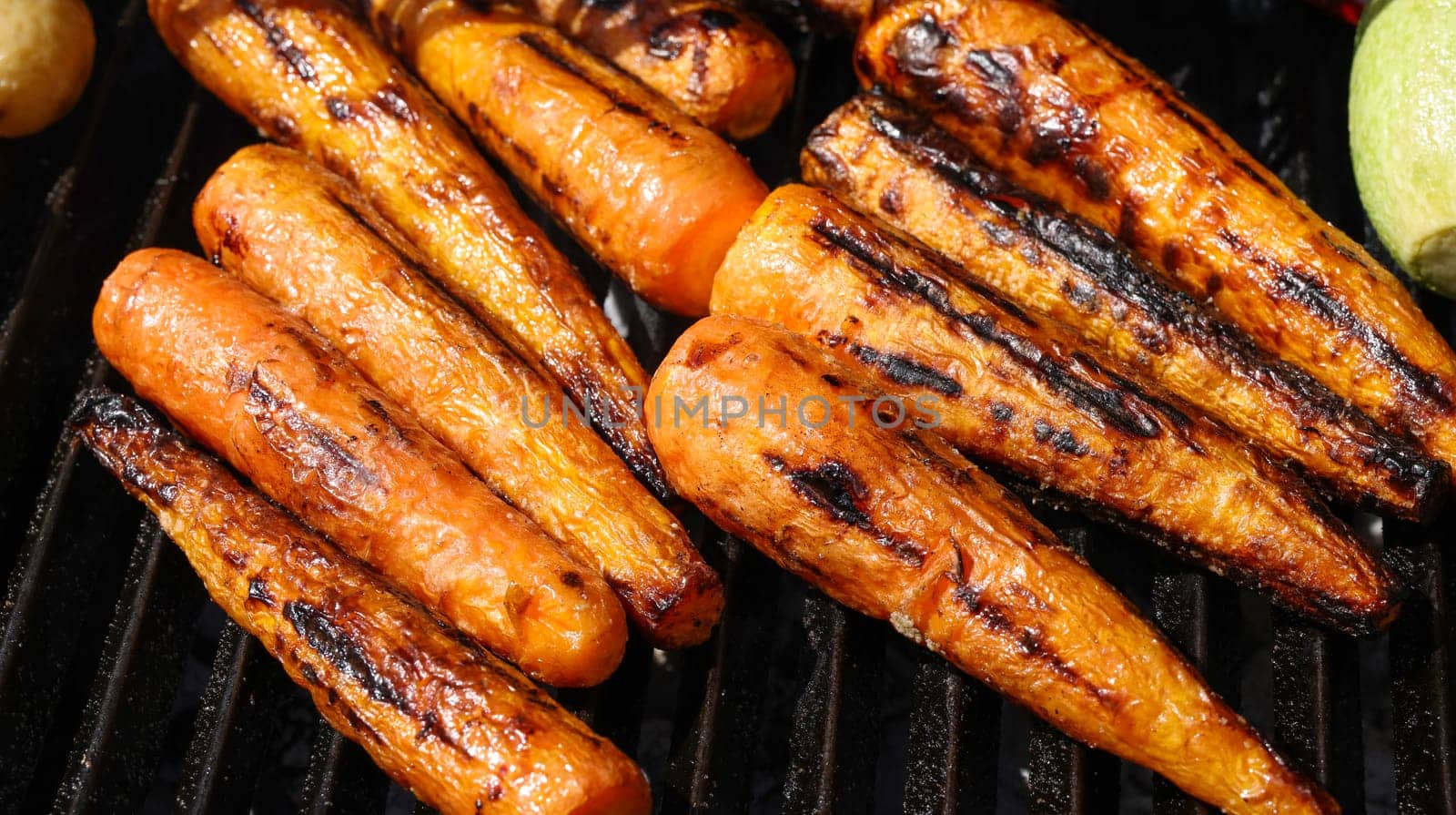Close up cooking fresh new carrots in outdoor charcoal grill with cast iron metal grate, high angle view