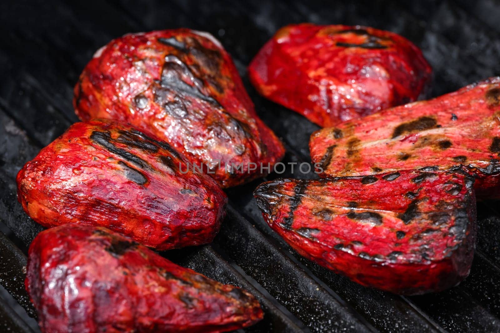 Close up cooking fresh new red beet roots in outdoor charcoal grill with cast iron metal grate, high angle view