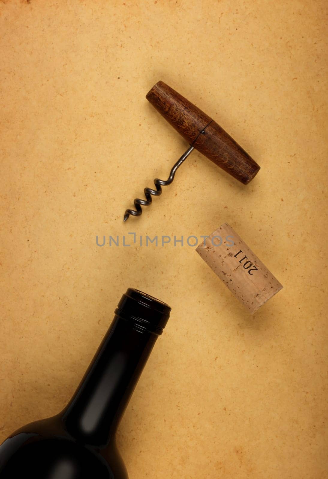 Close up one full unopen bottle of red wine with cork and retro opener with wooden handle over vintage brown paper background with copy space, high angle view