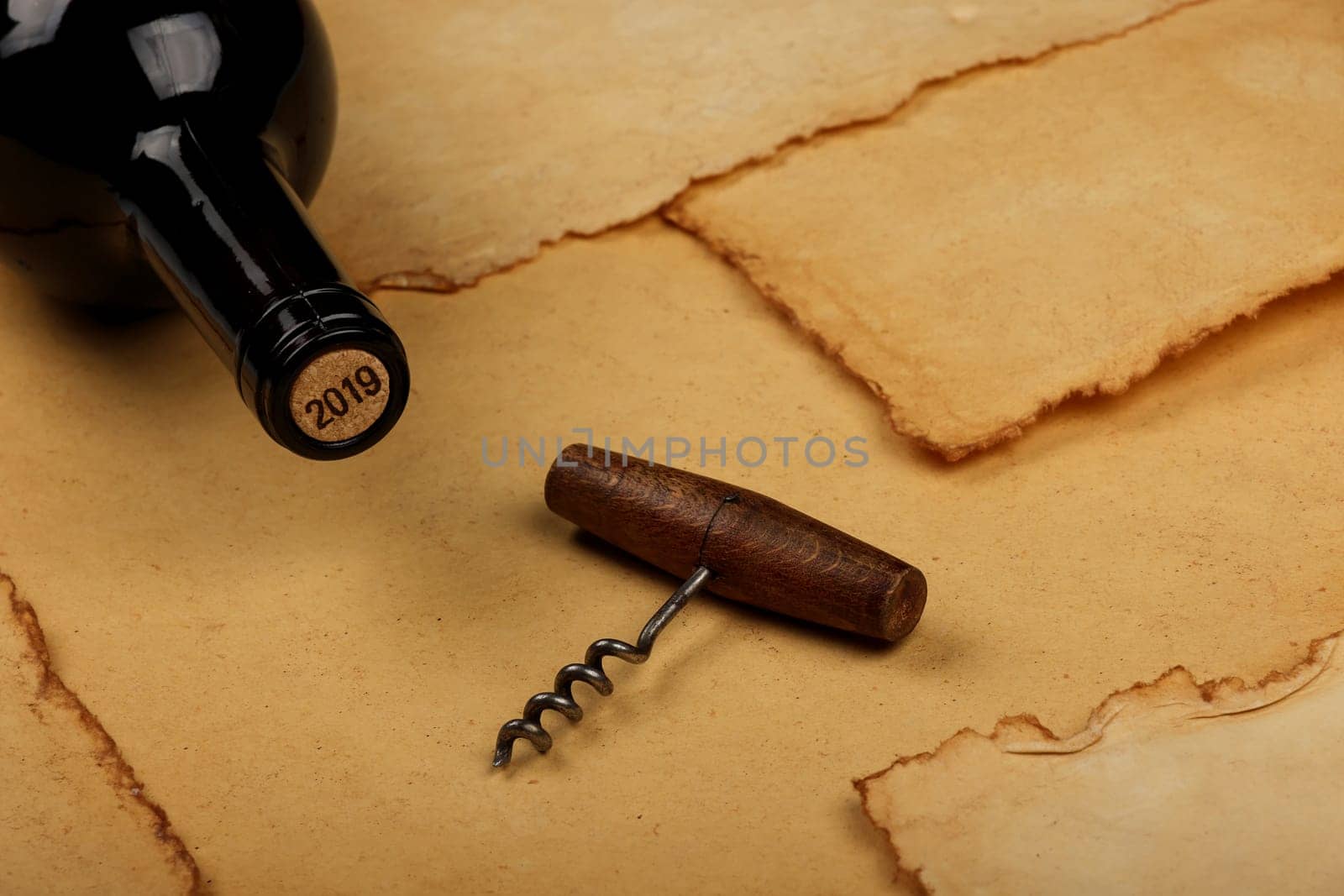 Close up one full unopen bottle of red wine with cork and retro opener with wooden handle over vintage brown paper background with copy space, high angle view