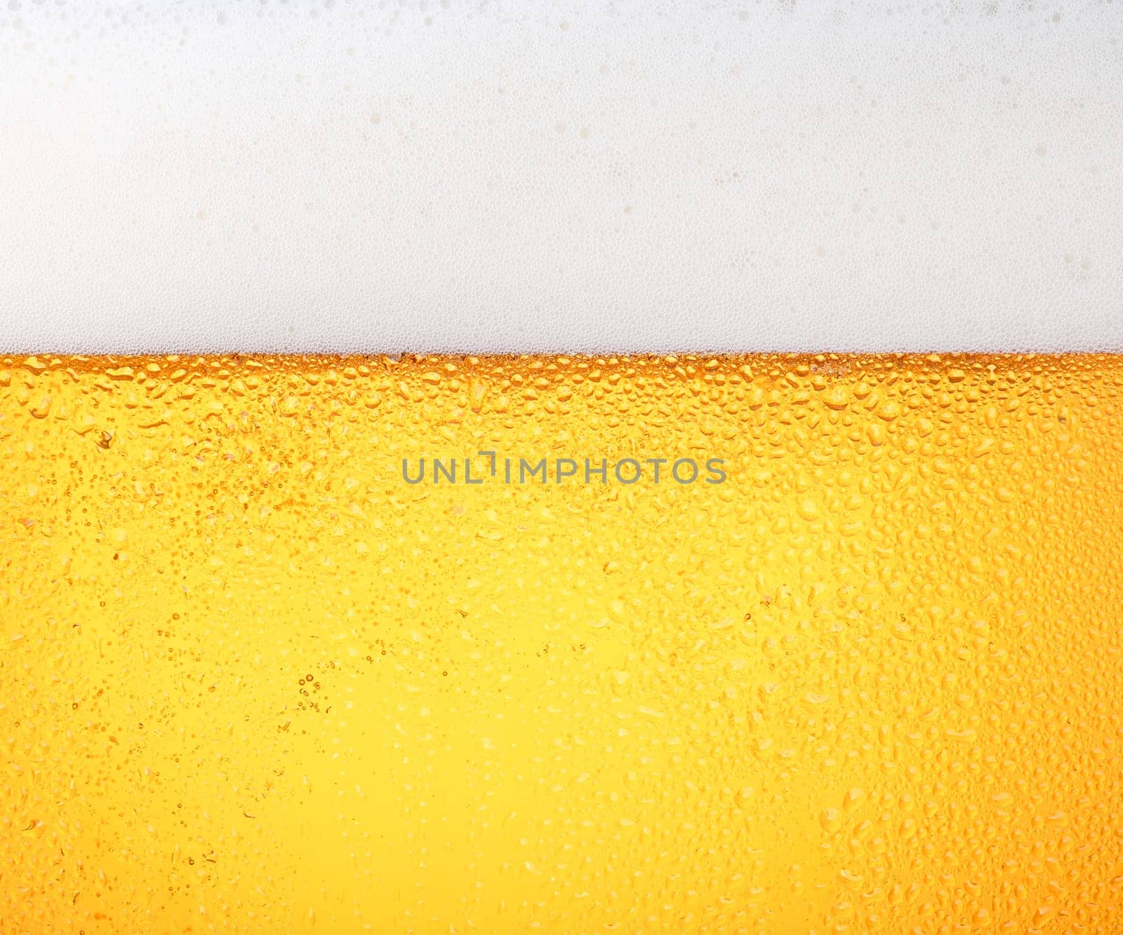 Close up background texture of pouring lager beer with bubbles and froth in frosty glass with drops, low angle side view