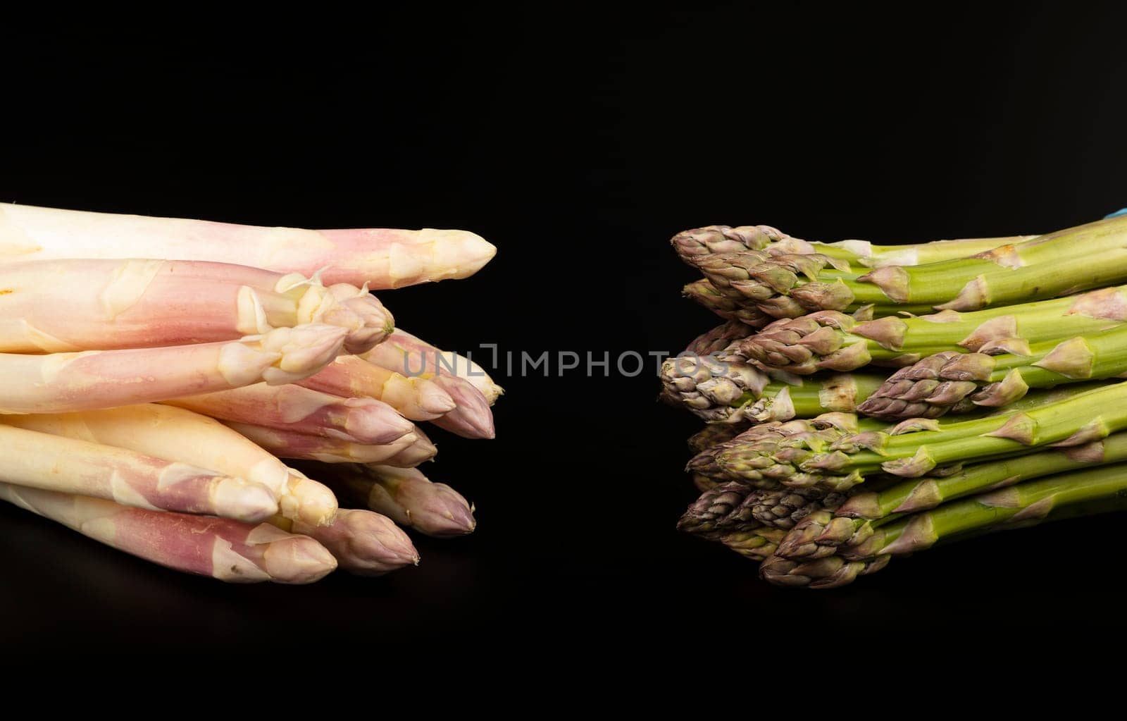 Close up two bunches of fresh white and green asparagus compared isolated on black background, high angle view