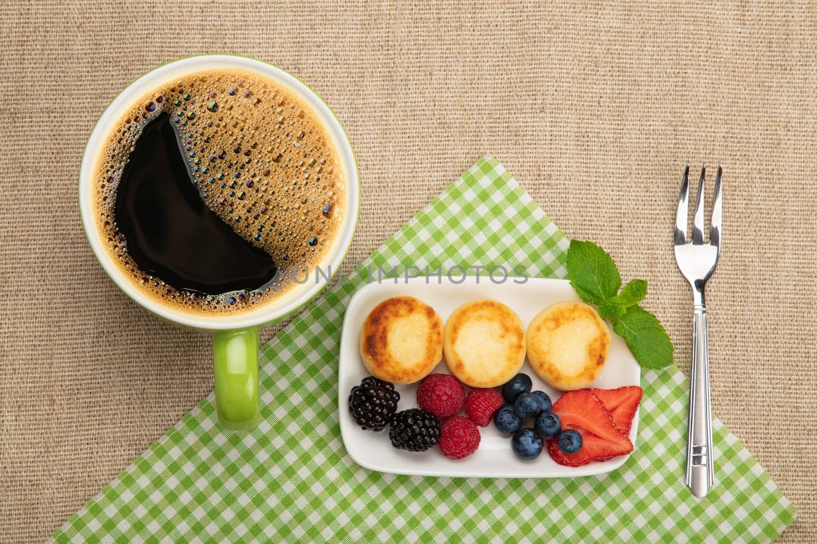 Close up serving portion of European quark cheese pancakes dessert with fruits and cup of black coffee, elevated top view, directly above