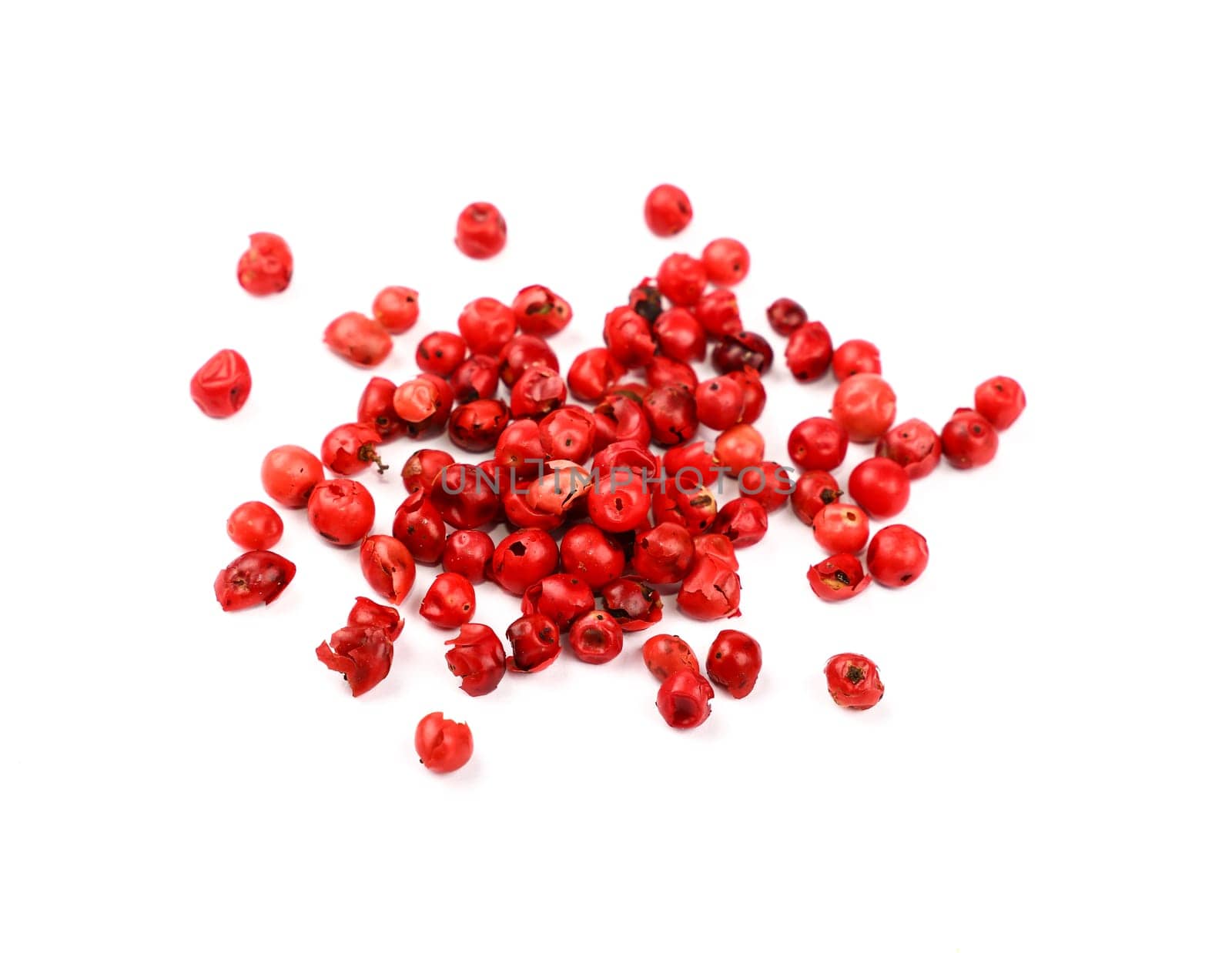 Close up heap of red pink pepper peppercorns spilled and spread around isolated on white background, high angle view