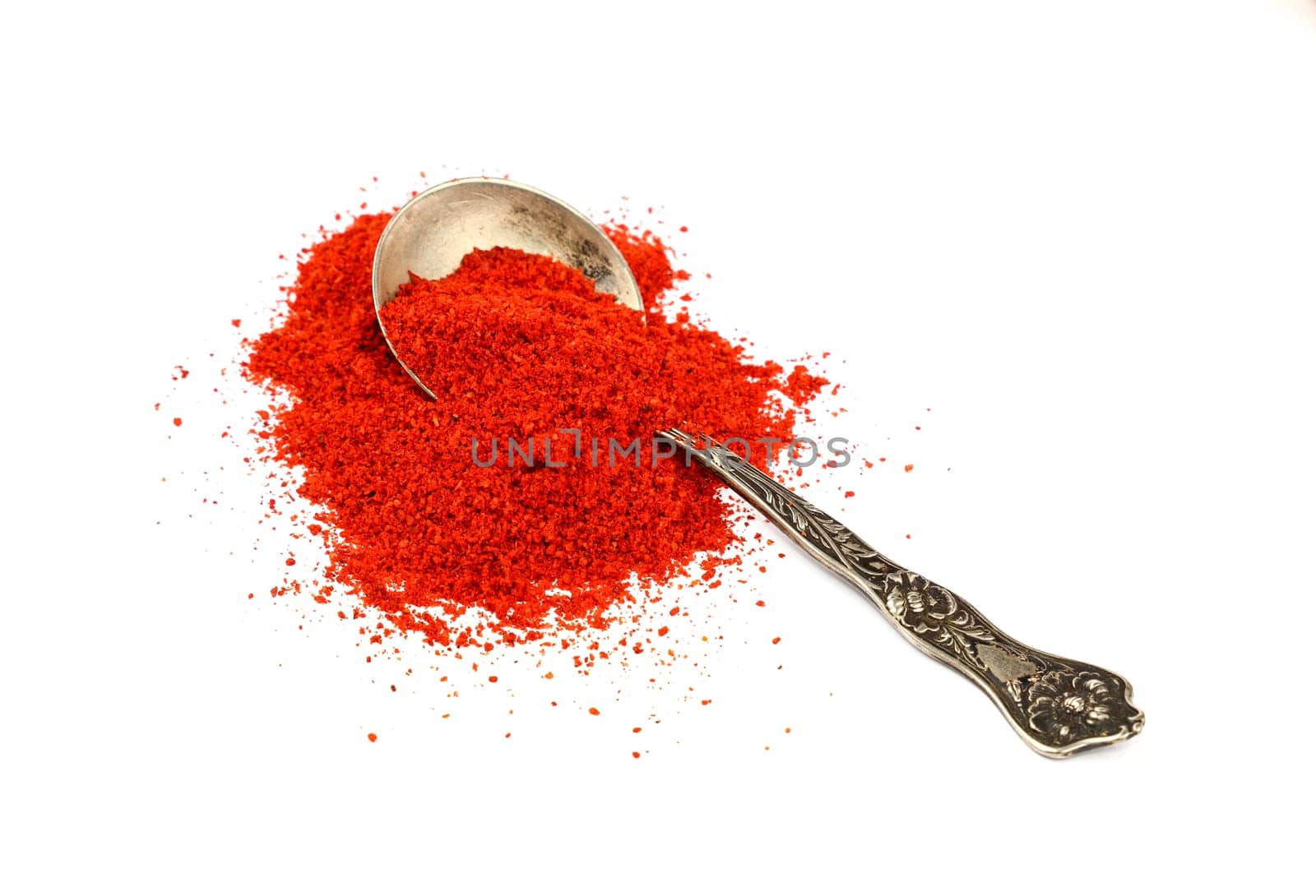 Close up one vintage metal spoon full of red chili pepper, paprika or sundried tomato powder spilled and spread around isolated on white background, elevated top view, directly above