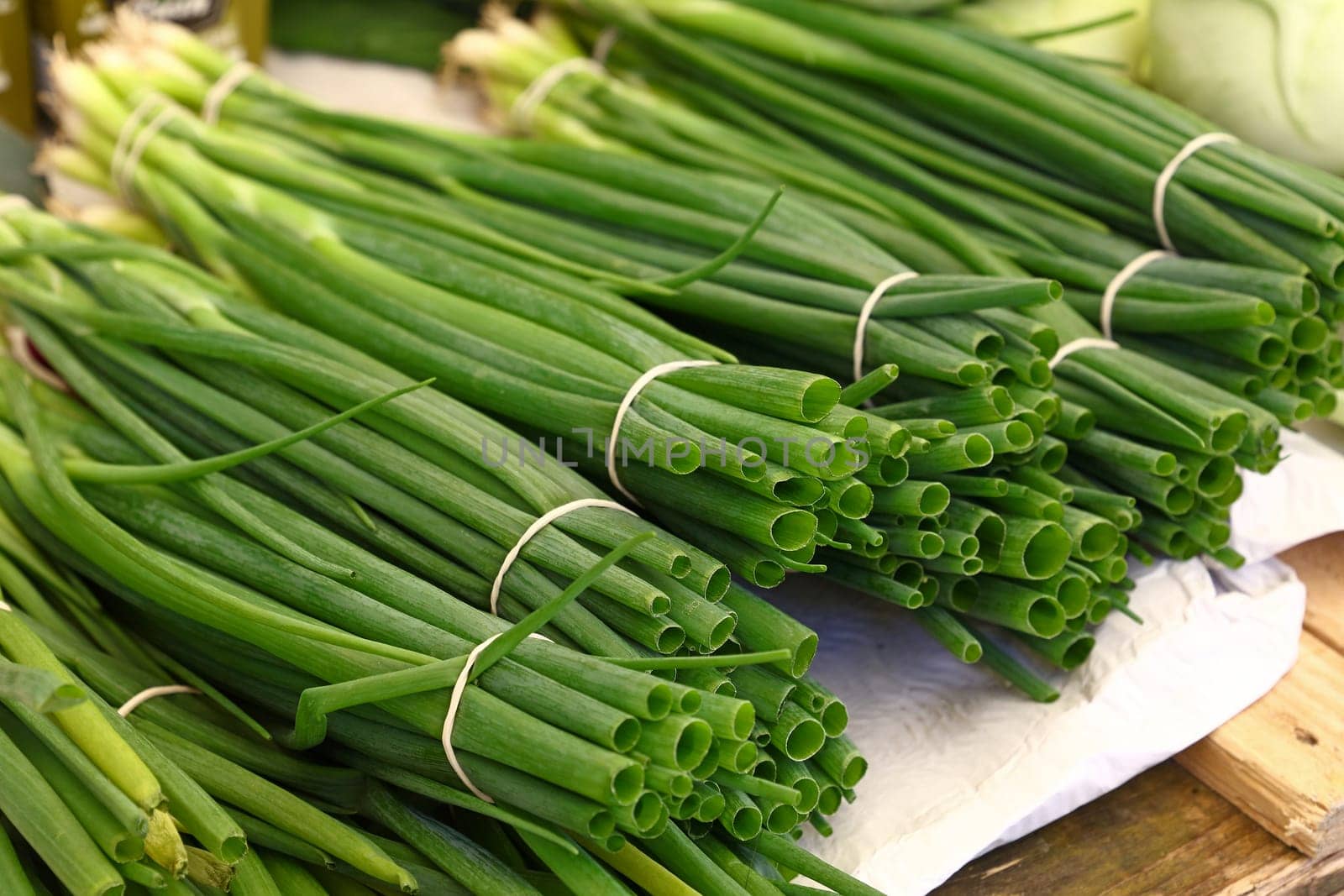 Heap of fresh green spring bunch onion, scallion or chive on farmers market display, close up, high angle view