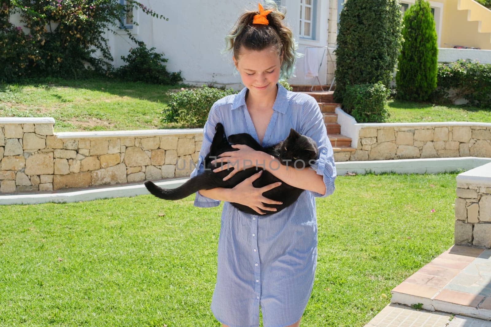 Running teenager girl holding beautiful black cat in her arms, sunny summer day