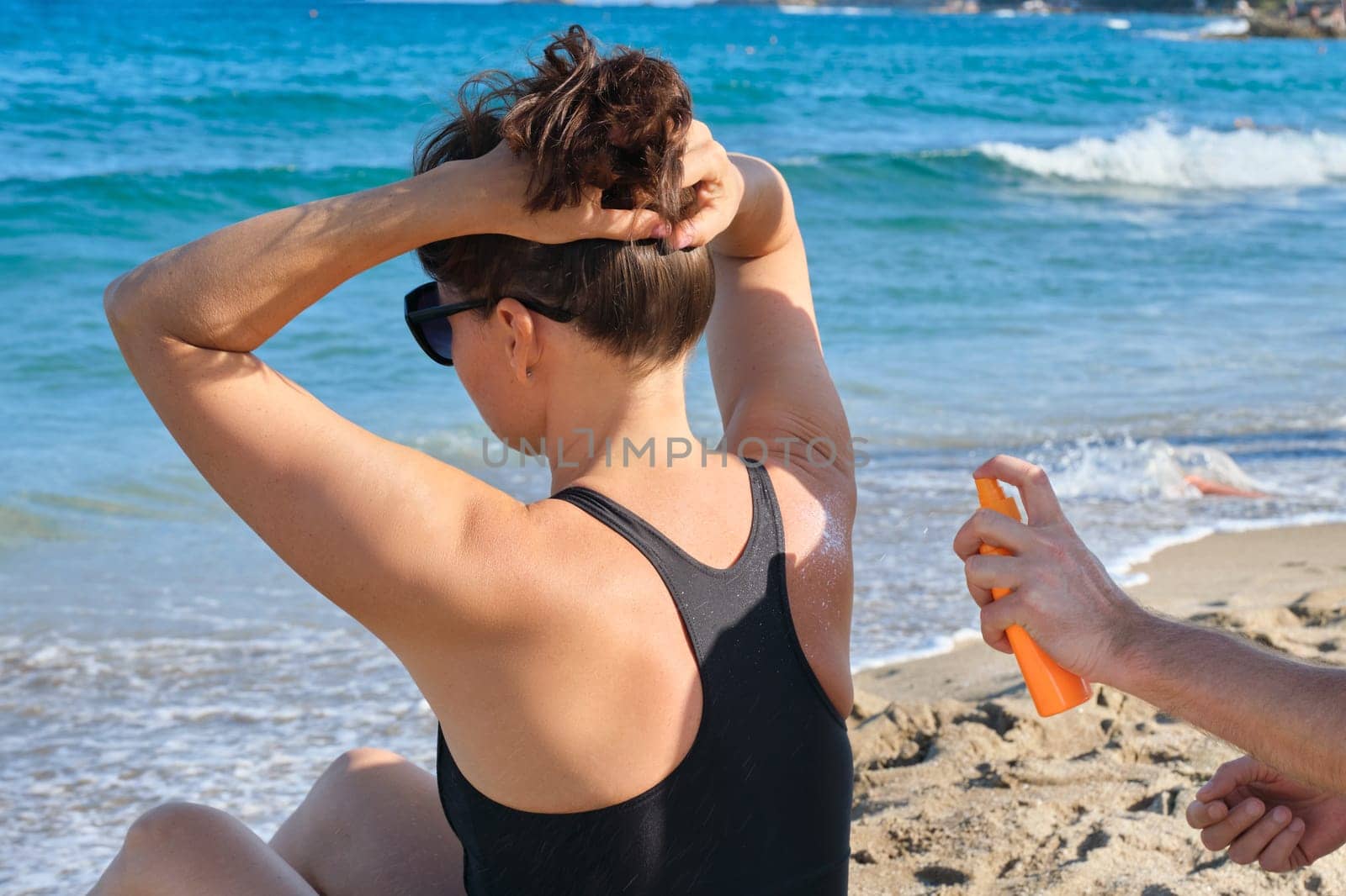 Mans hands applying sun protection cream to mature womans skin by VH-studio