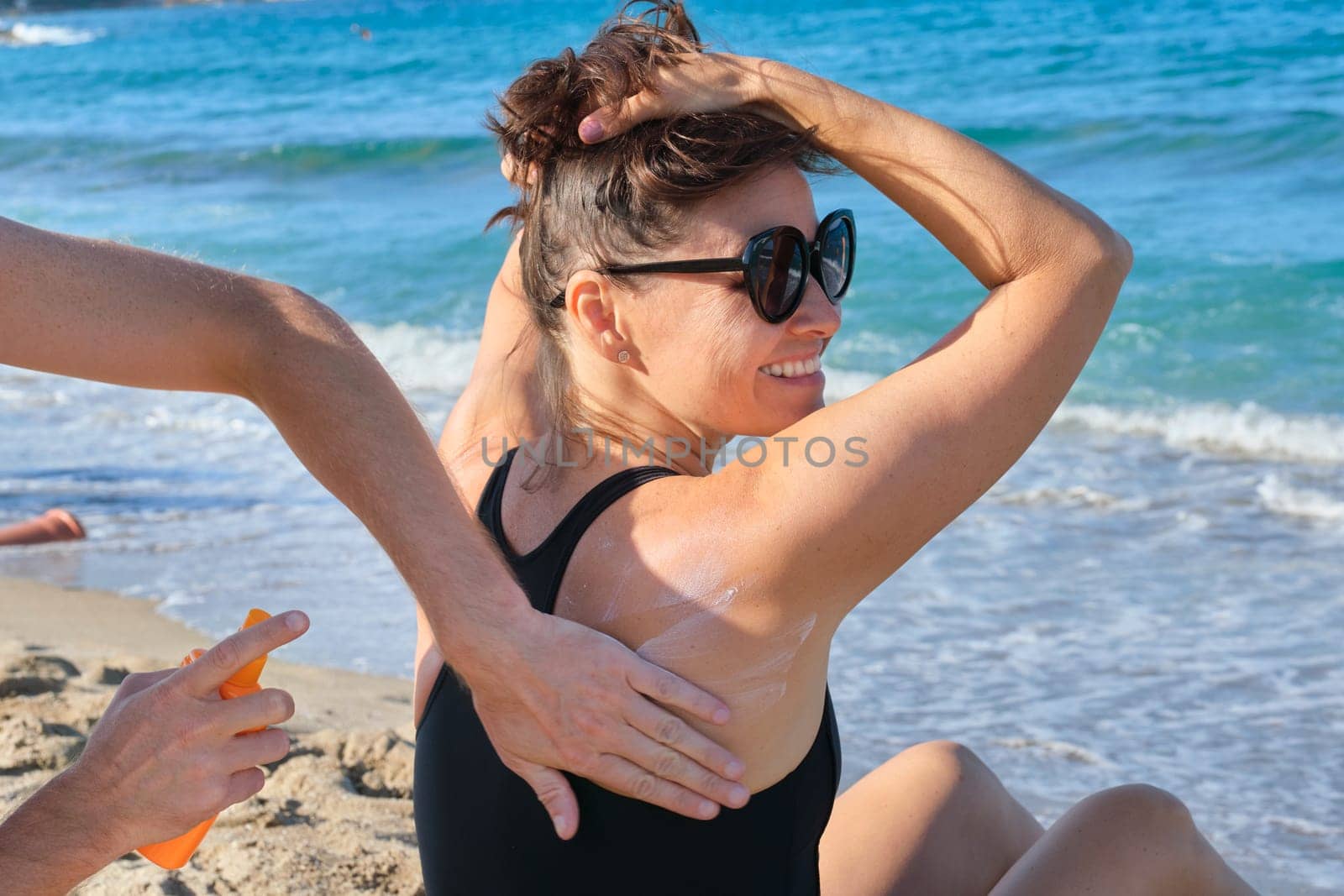 Middle-aged woman on the beach, male hands applying sun-shaped cream.