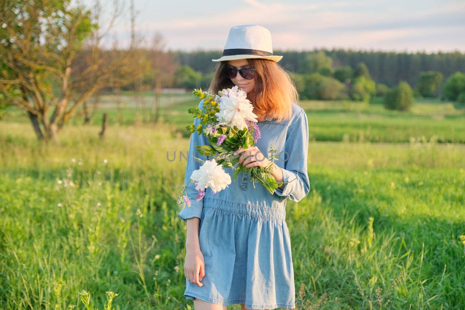 Beautiful teenager girl in jeans dress hat with bouquet of wildflowers, background scenic landscape, beauty, nature, copy space