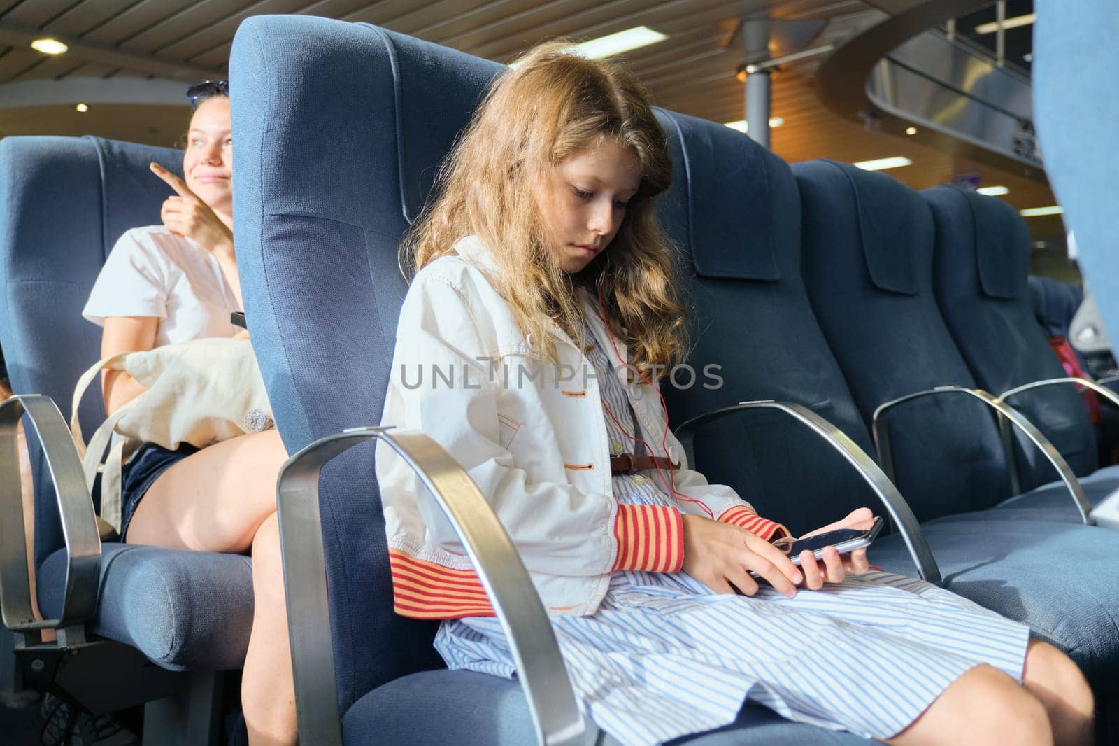 Girl child using smartphone while sitting inside ferry. Travel, tourism, transportation by water