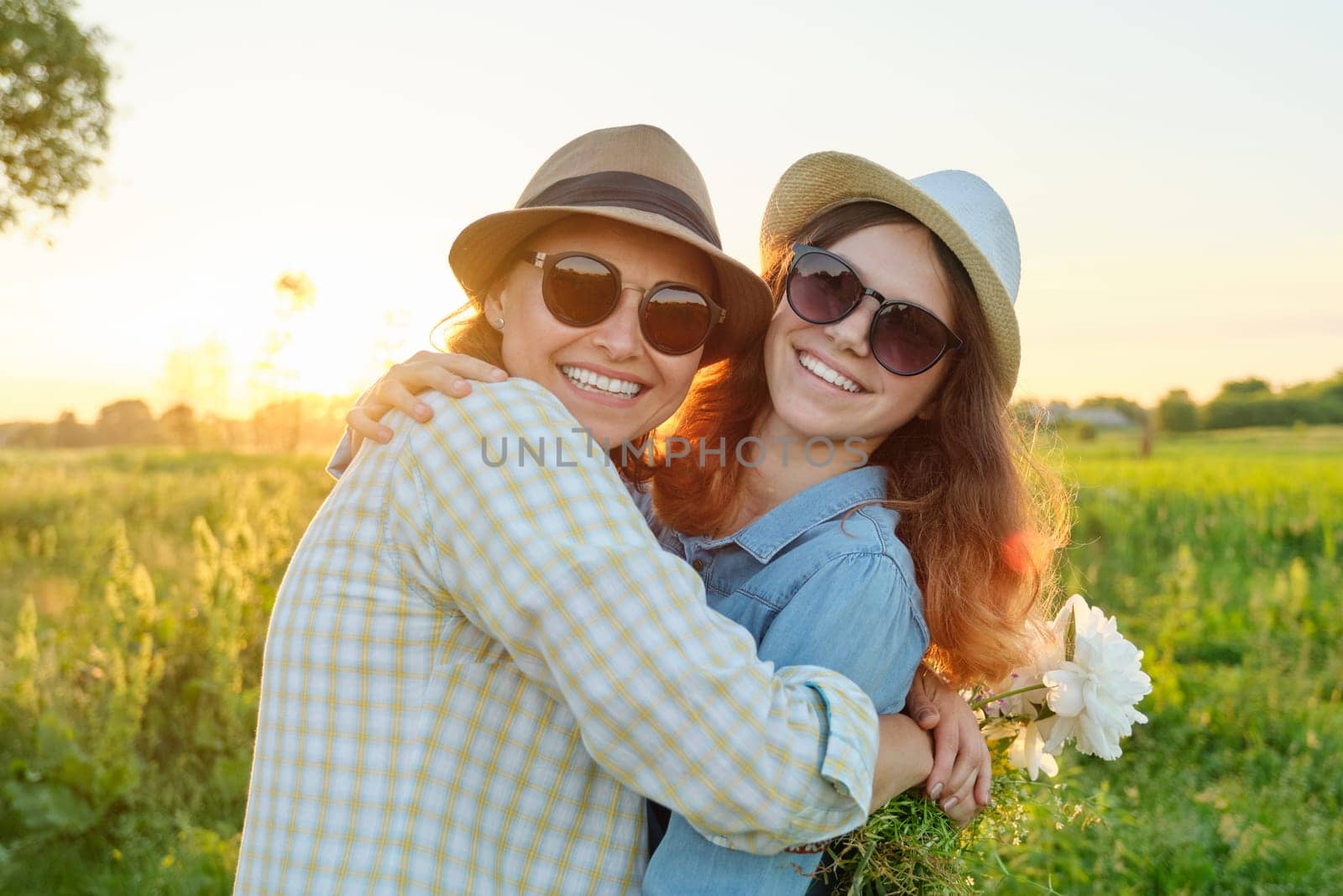 Mothers day, hugging happy smiling teenager daughter with mother in meadow with bouquet of spring flowers