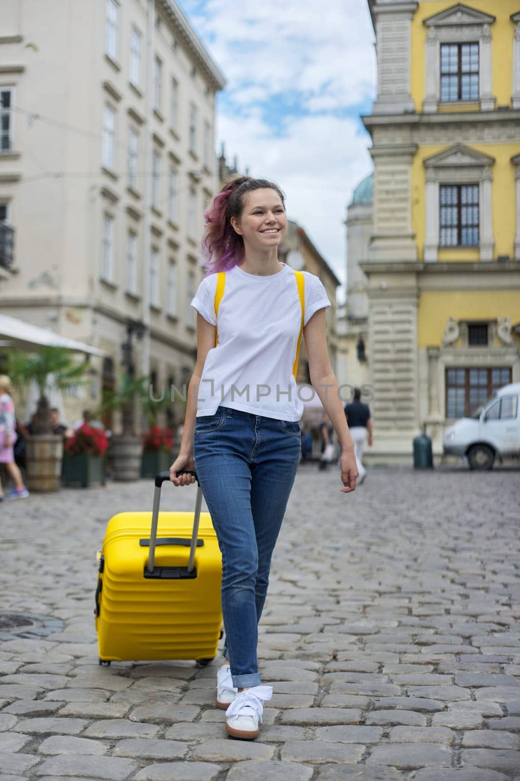 Girl teenager student walking with backpack and yellow suitcase on city street. Start of studies, vacation, journey