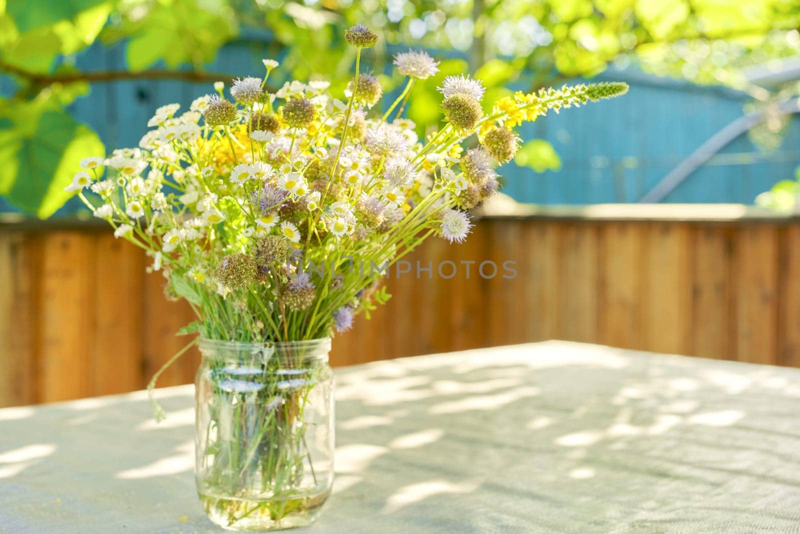 Bouquet of summer wildflowers and herbs in jar on table on terrace, sunny day, rustic style