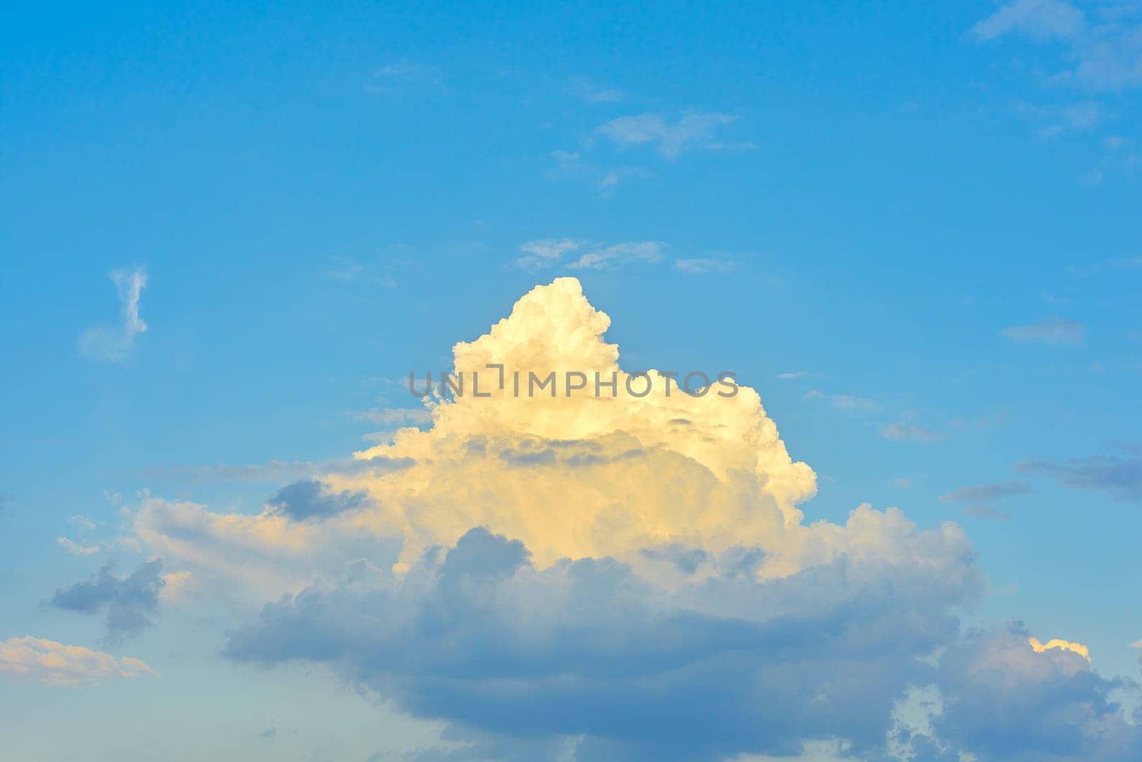 Single bright white dreamlike cloud on a blue dramatic sky. One cloud backlit by the sun
