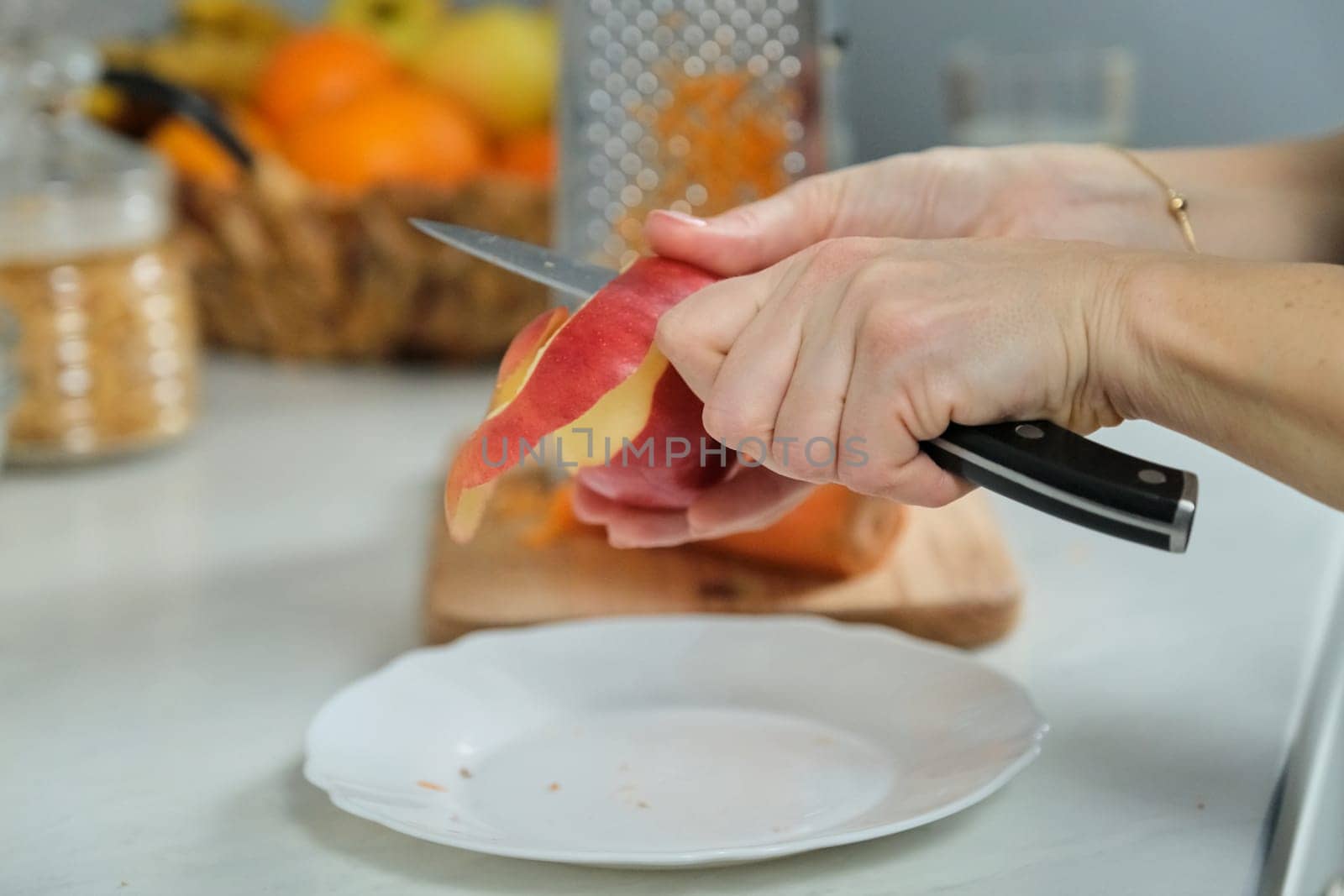 Cooking food at home in the kitchen, closeup of womans hand with knife cutting an apple skin