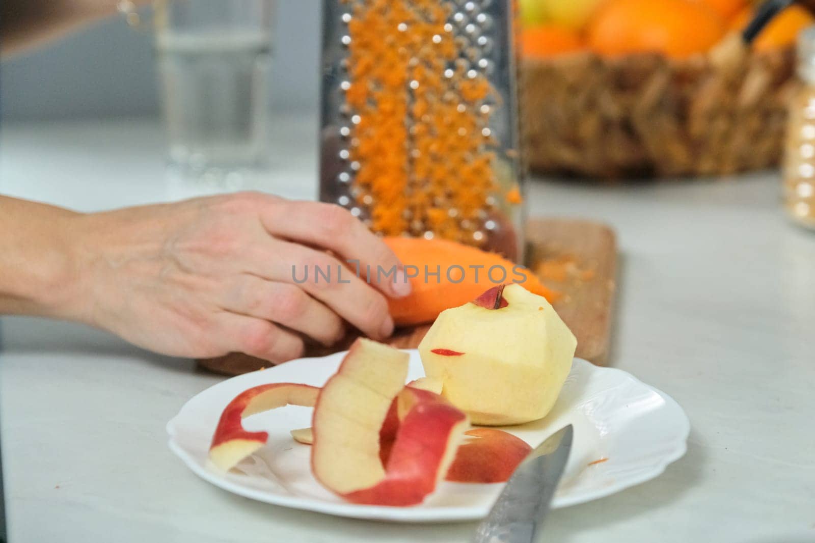 Cooking food at home in the kitchen, close-up of womans hand with grater, rubbing an apple carrot.