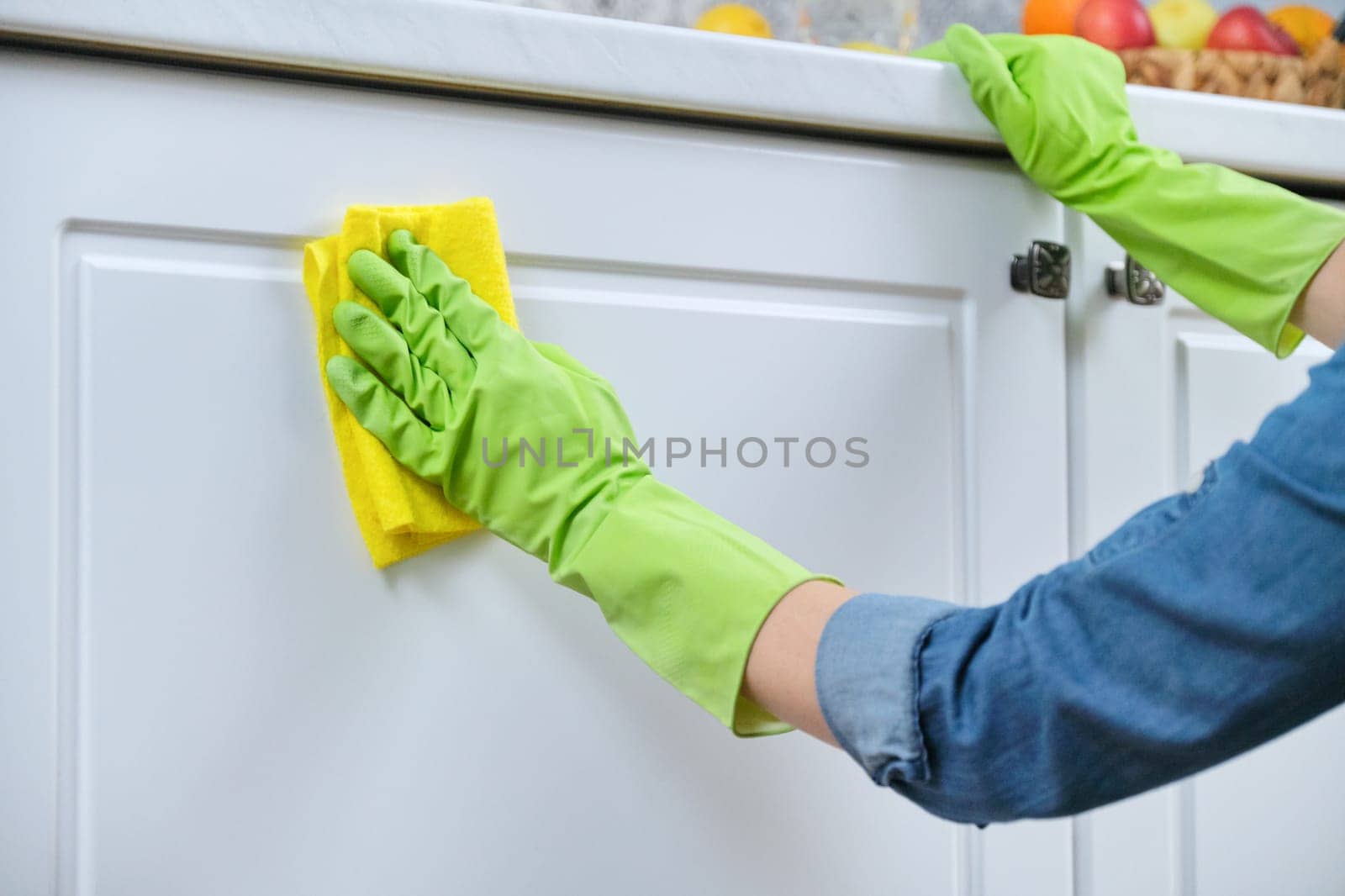 Woman in gloves with rag washing, cleaning, polishing furniture doors on kitchen, cleaning house