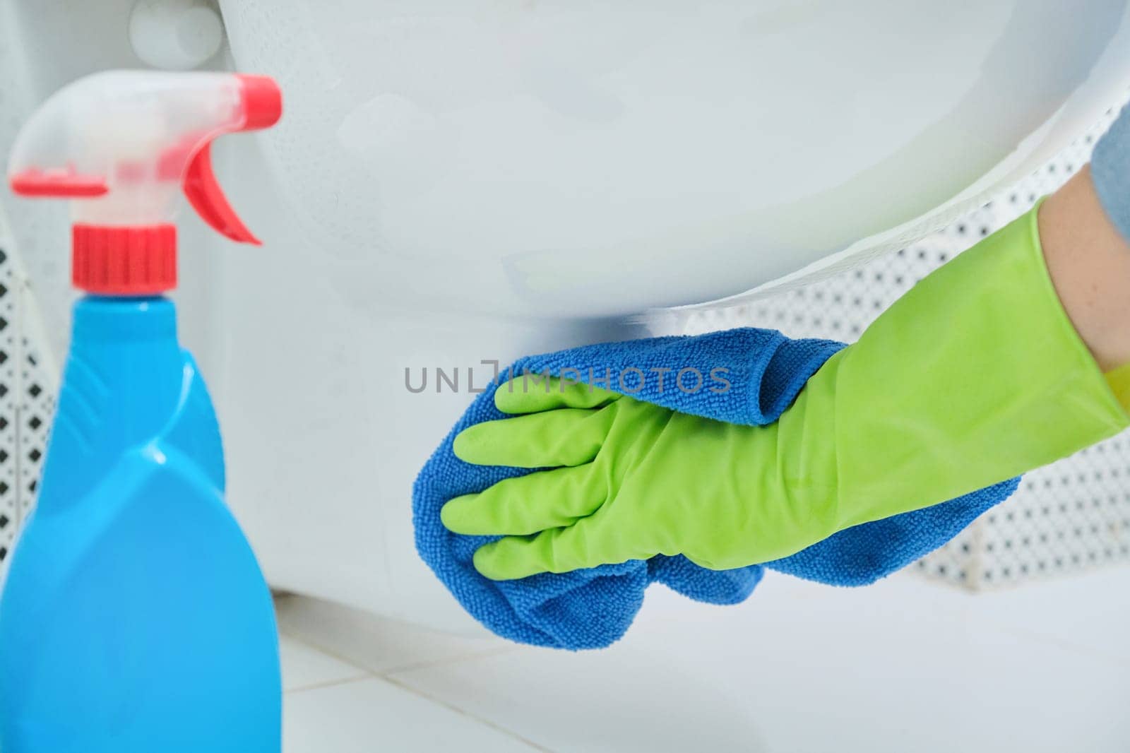 Close-up of woman hand in gloves with rag and detergent washing hanging toilet, home cleaning in bathroom