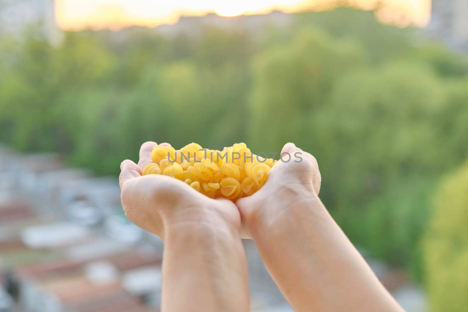 Spiral pasta, close-up of hands holding pasta, background sunset sky golden hour
