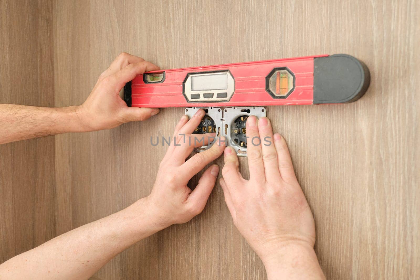 Repair and installation of furniture, hands of electrician worker installing electrical outlet in furniture using screwdriver and level