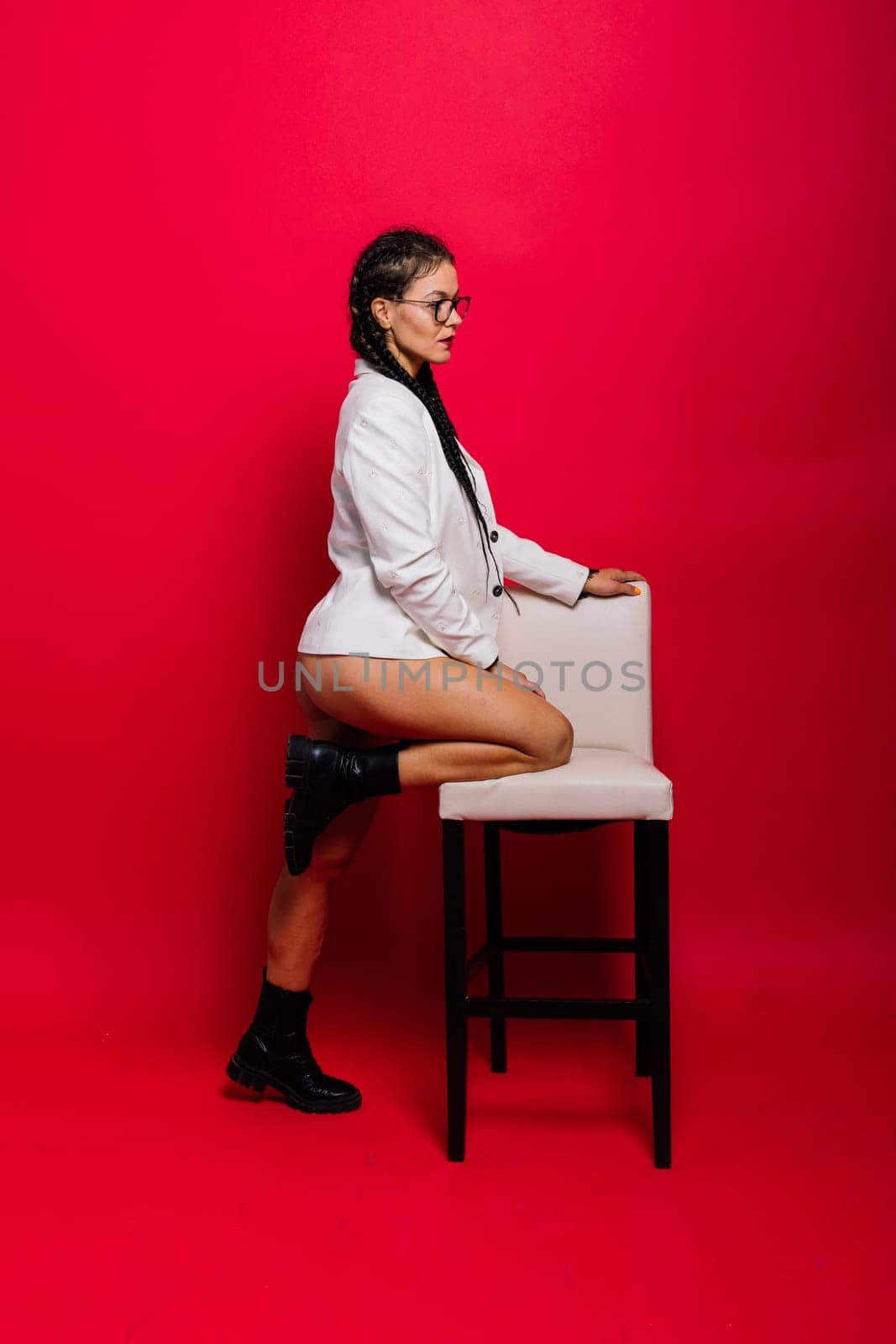 Beautiful female posing in a black underwear and white classic suit over red studio background.