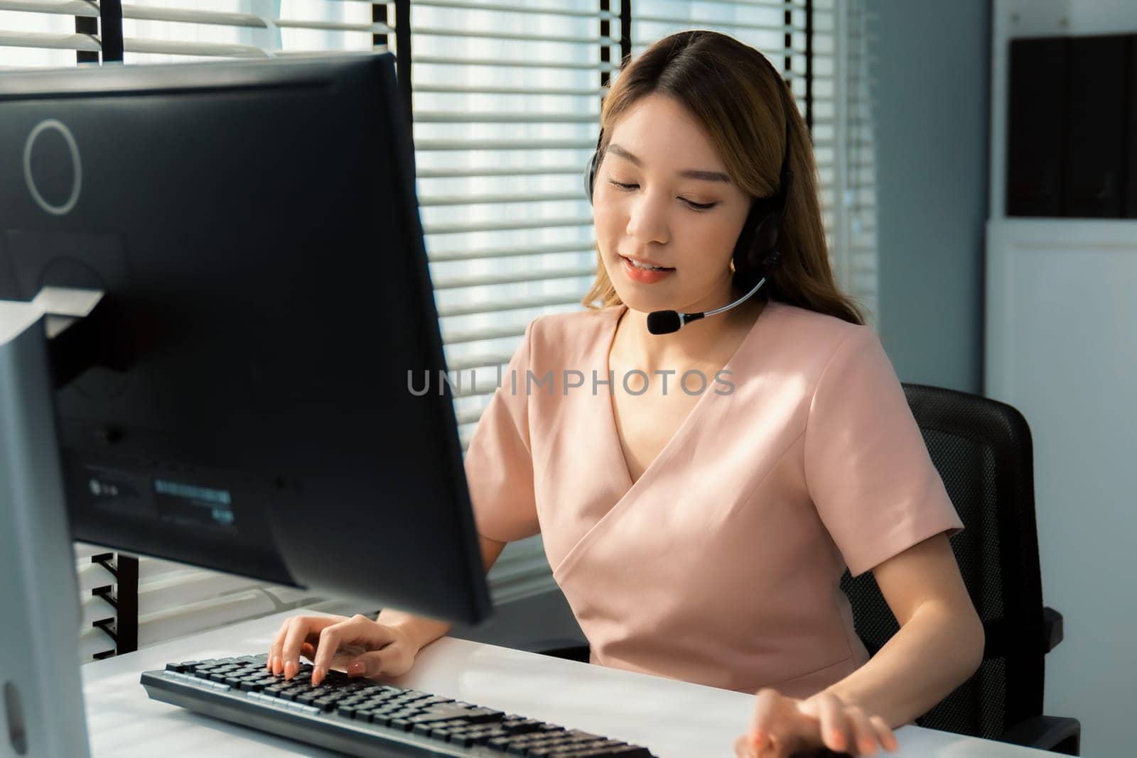 Competent female operator working on computer and while talking with clients. Concept relevant to both call centers and customer service offices.