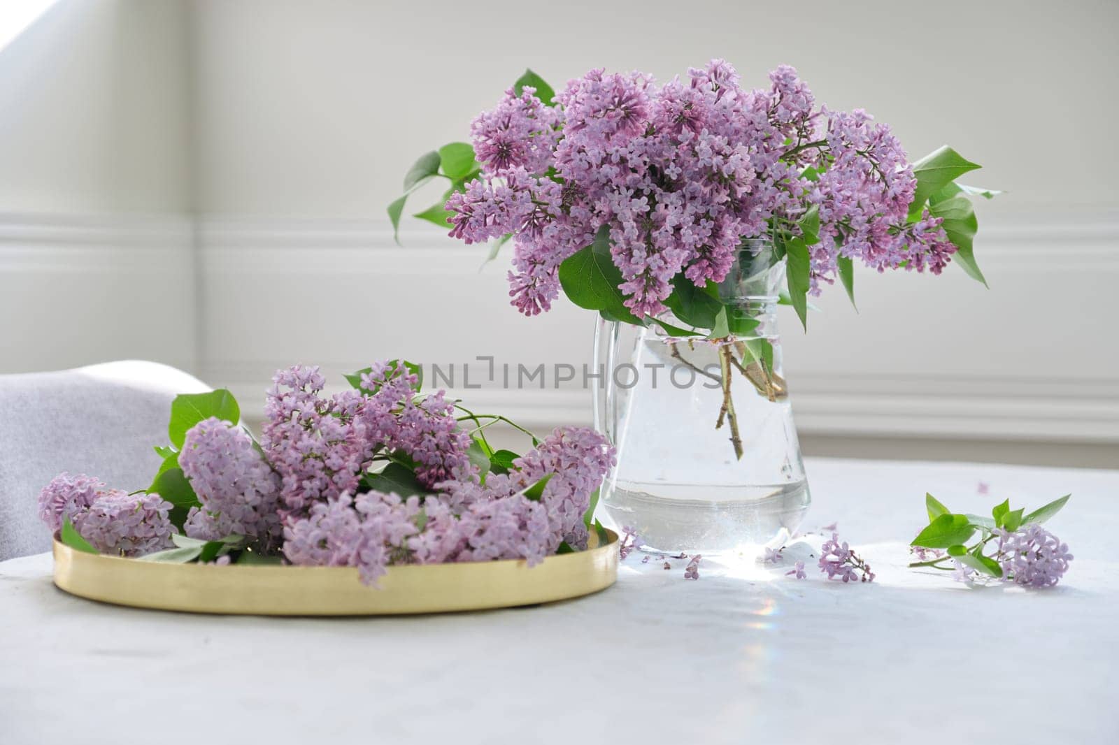 Spring bouquet of lilac flowers in glass jug on table, spring holidays, sunny mood, background white tablecloth