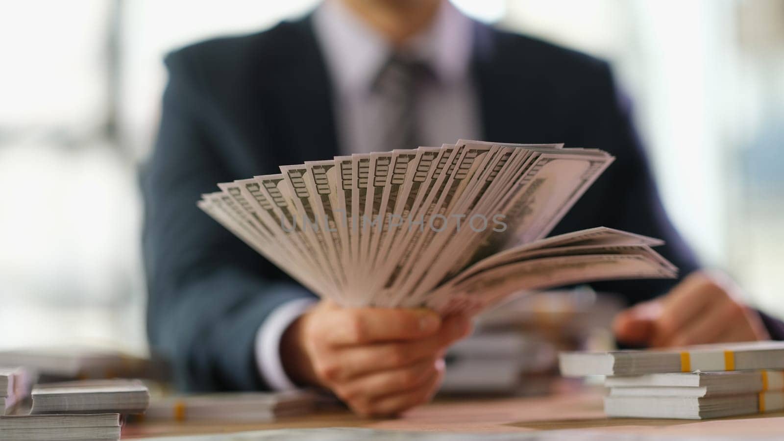 Businessman banker holding fan of dollar bills in hand closeup. High earnings in business concept