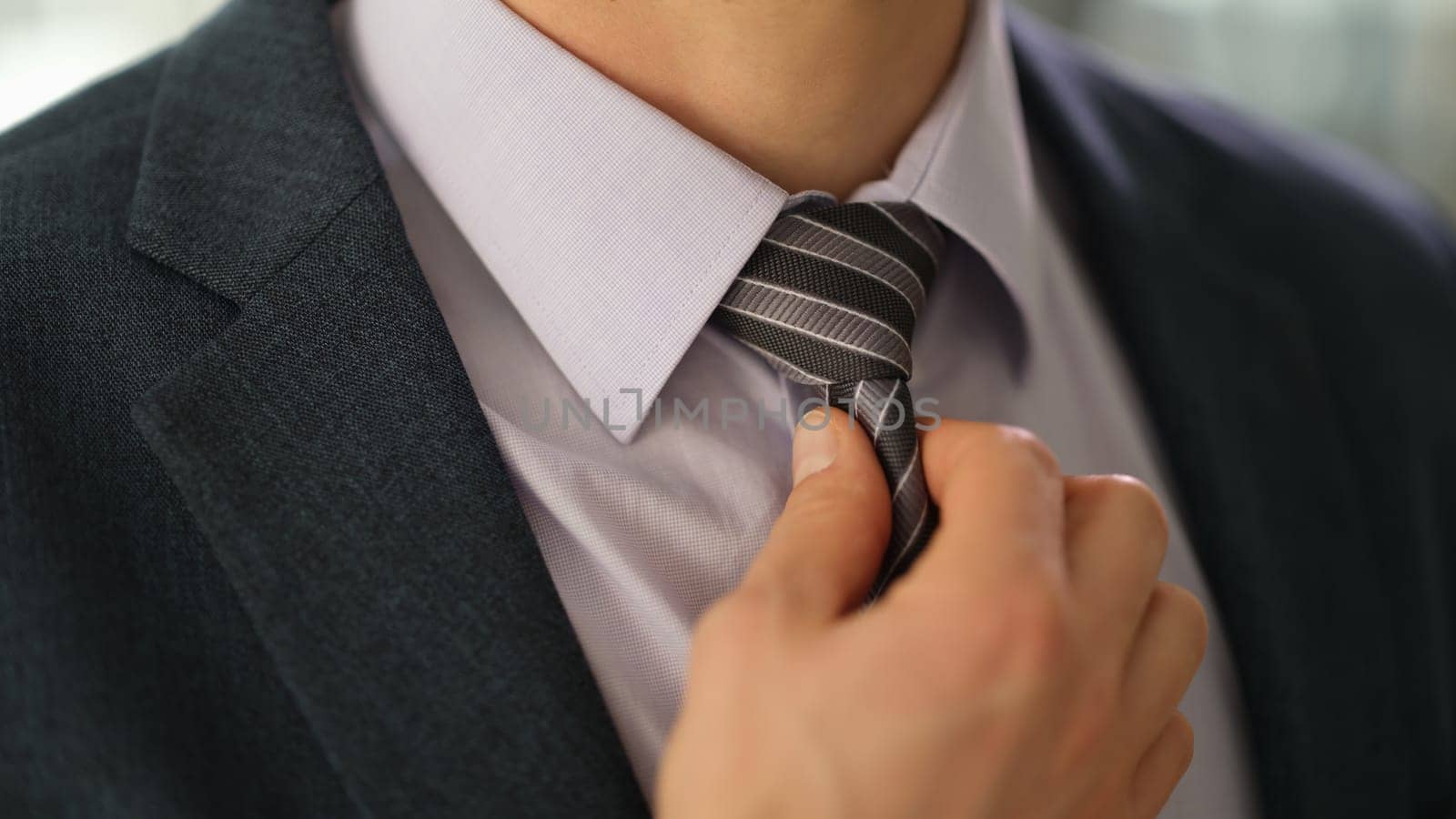 Elegant businessman in suit straightening tie on shirt closeup by kuprevich