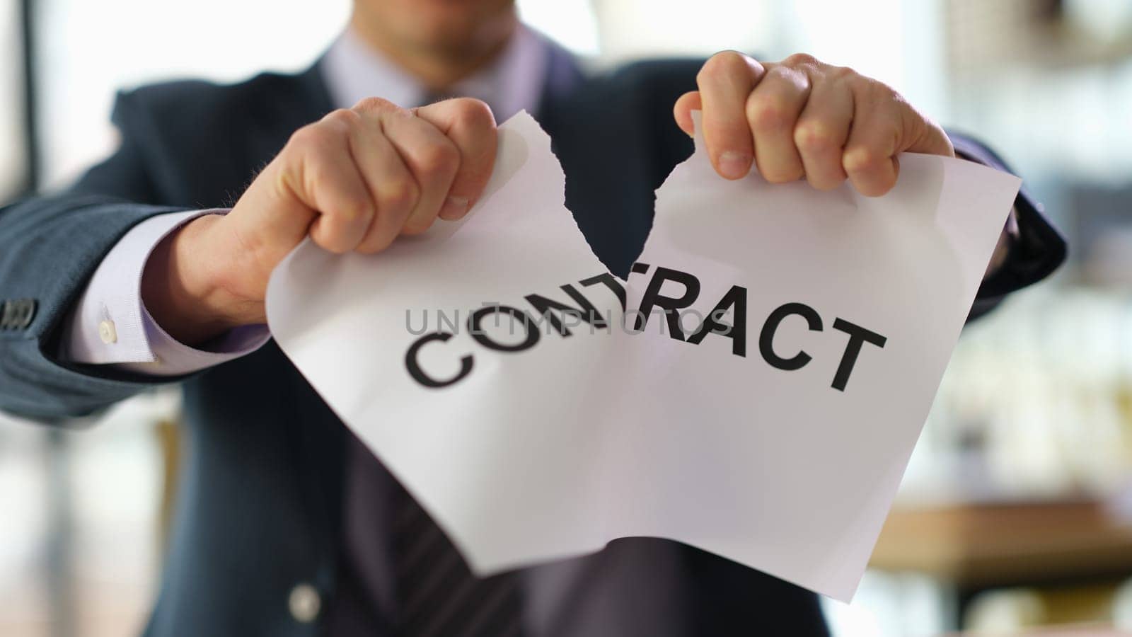 Businessman in suit tearing paper document contract at work in office closeup. Broken or breached contract violation of labor obligations concept