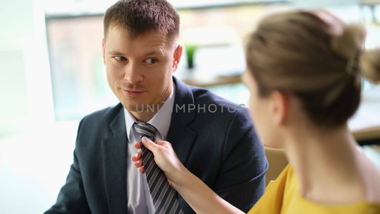 Woman secretary straightening tie to manager man at work in office. Romantic relationship at work career growth concept