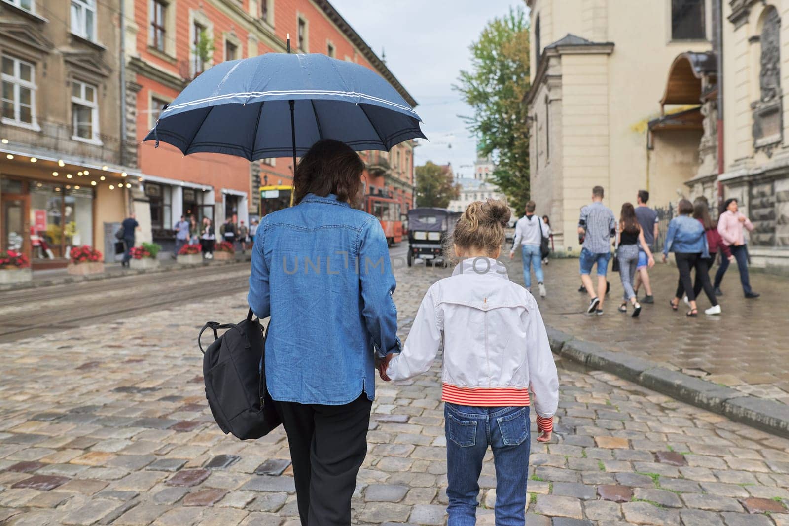 Woman with child girl walking under an umbrella in street by VH-studio