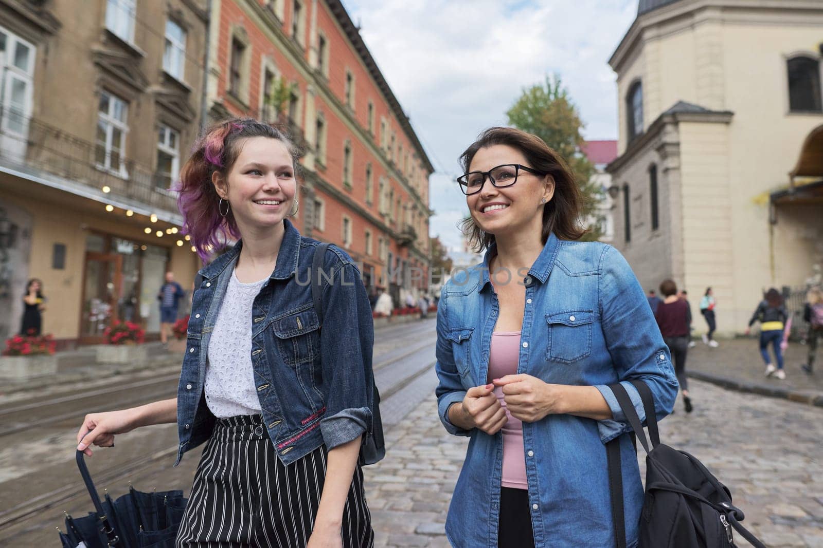 Portrait of mother and daughter of teenager 15 years old, walking and talking on city street