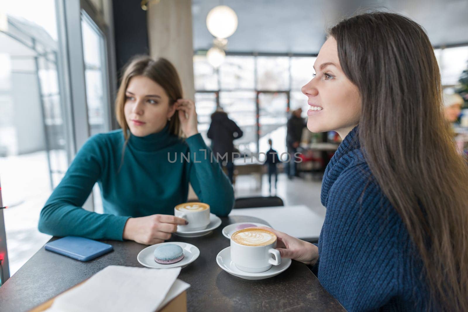 Two young beautiful women in cafe with cup of coffee talking in the break, season winter autumn