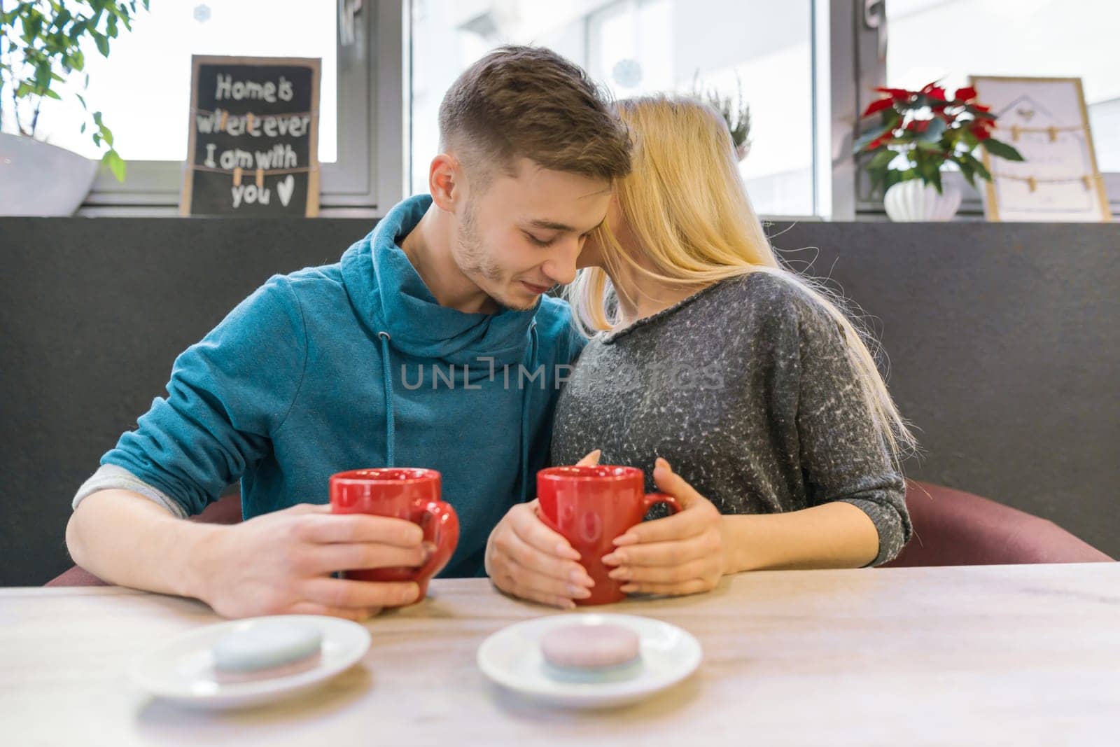 Young happy couple in love in cafe, man and woman together smile hugging, drinking coffee tea eating macaroons