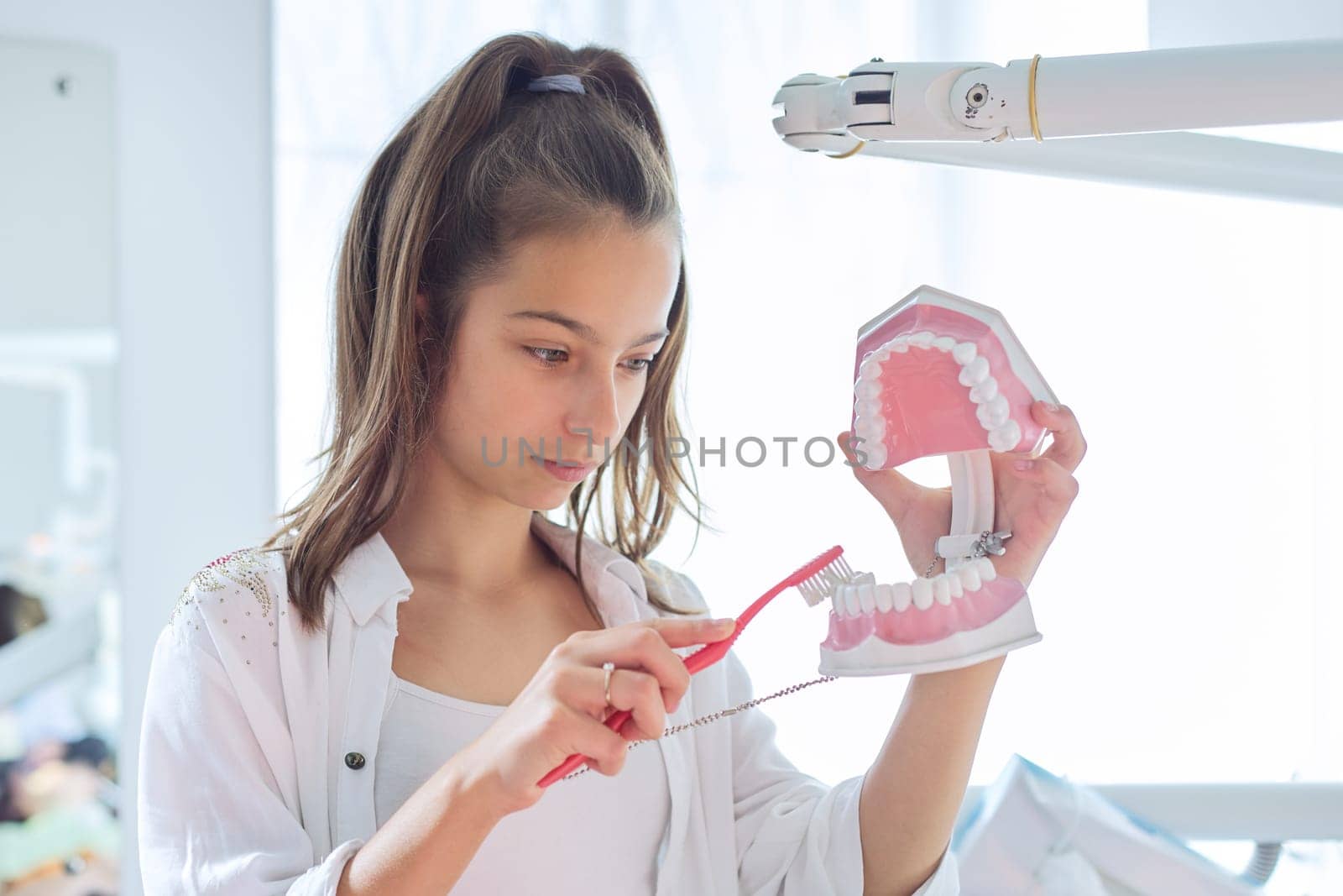 Smiling teenager girl in dental office holding jaw model with teeth in her hands