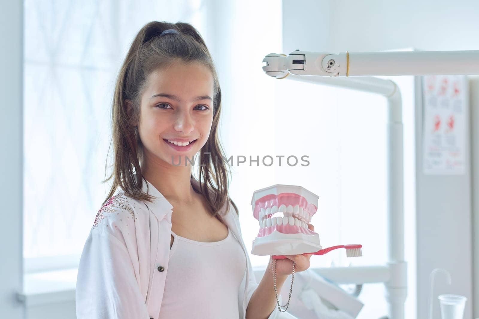 Smiling teenager girl in dental office holding jaw model with teeth in her hands