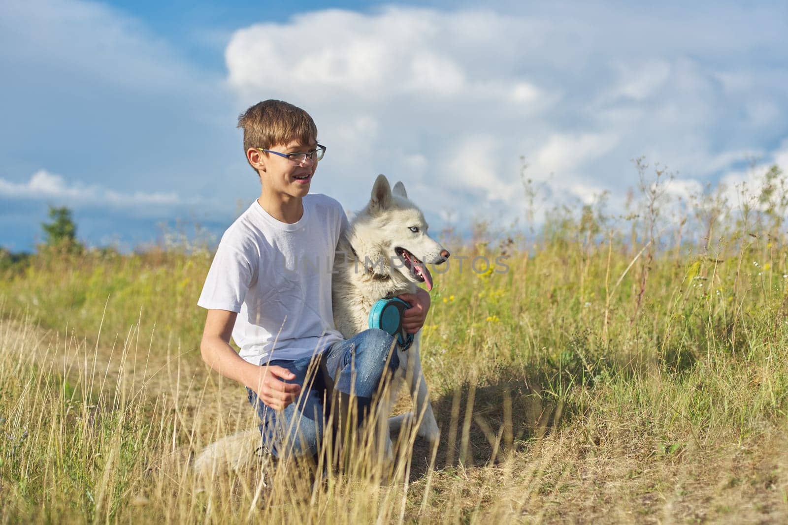 Boy with white dog, teenager walking with husky pet, background landscape with cloudy sky, yellow burnt grass