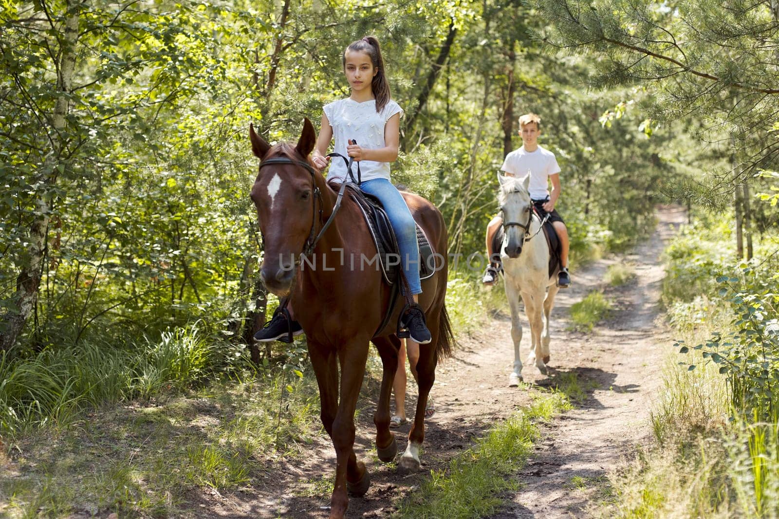 Group of teenagers on horseback riding in summer park.