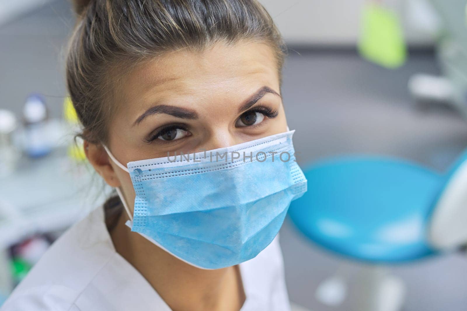 Closeup portrait of smiling female dentist doctor in protective medical mask at workplace dental clinic office, positive face