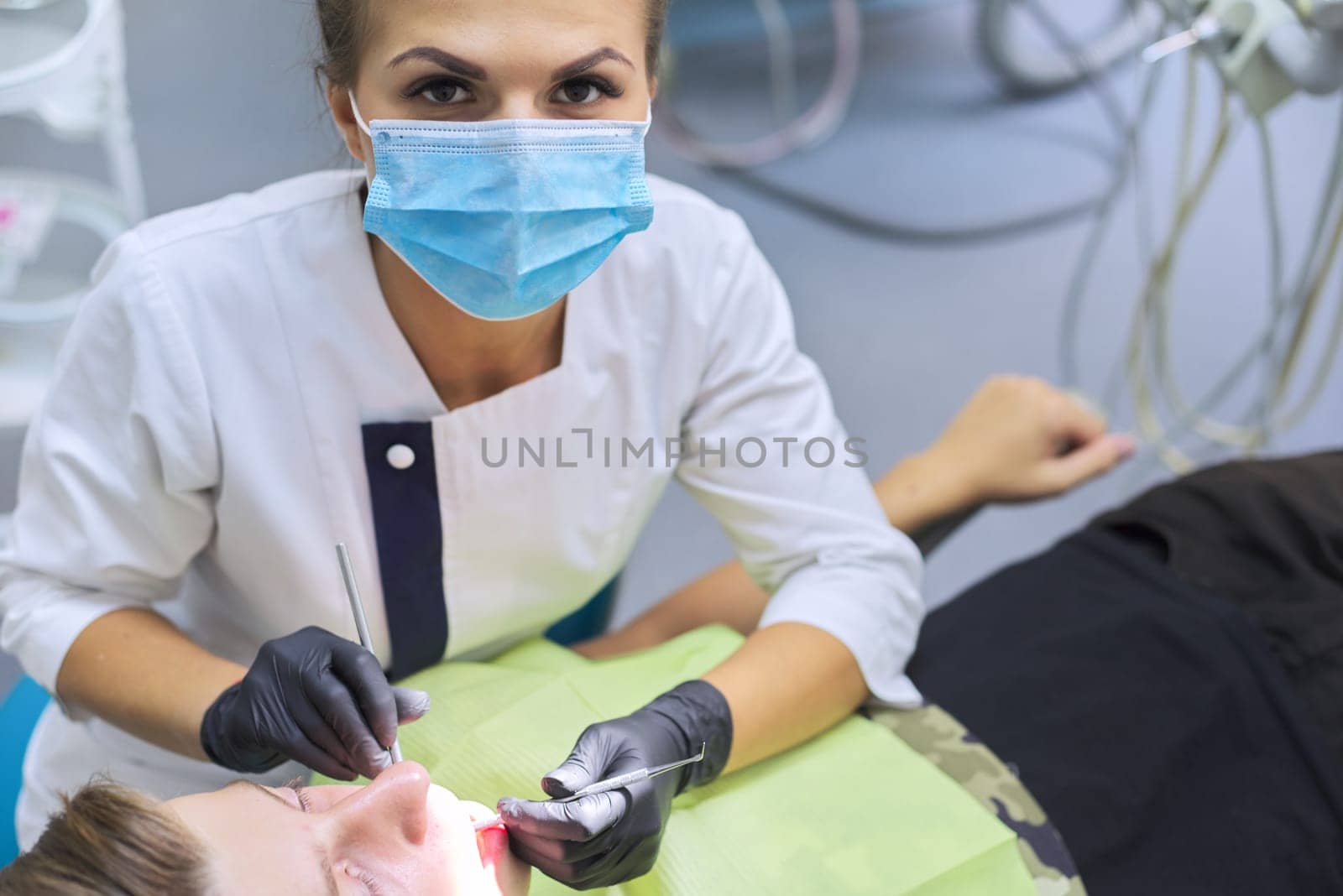 Female dentist treating teeth to patient, young man at dental clinic by VH-studio