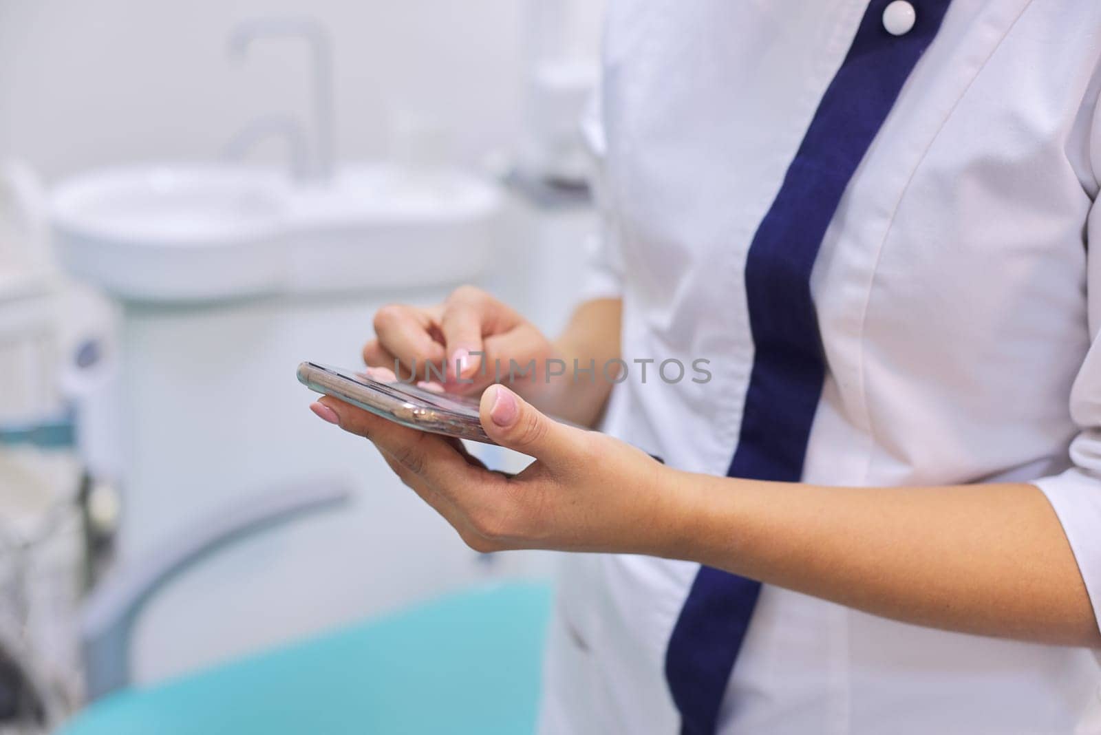 Close up of female doctors hand with mobile phone smartphone, dental clinic office background