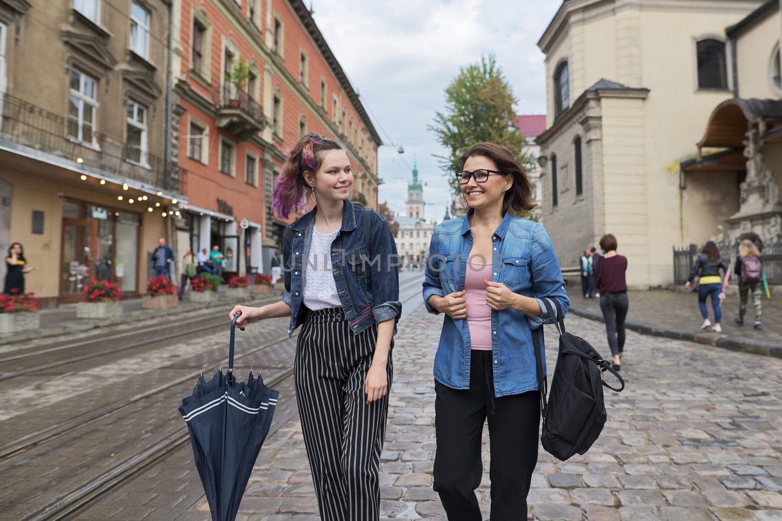 Mother and teenage daughter walking on city street, talking and smiling