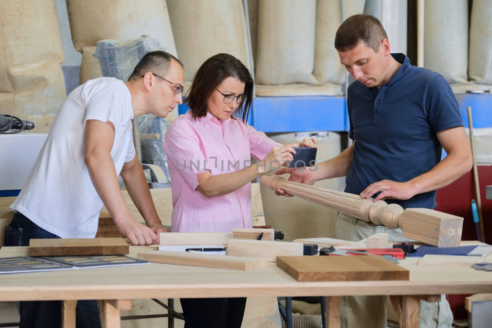 Group of industrial people client, designer or engineer and workers working together on project of wooden furniture. Teamwork in carpentry workshop.