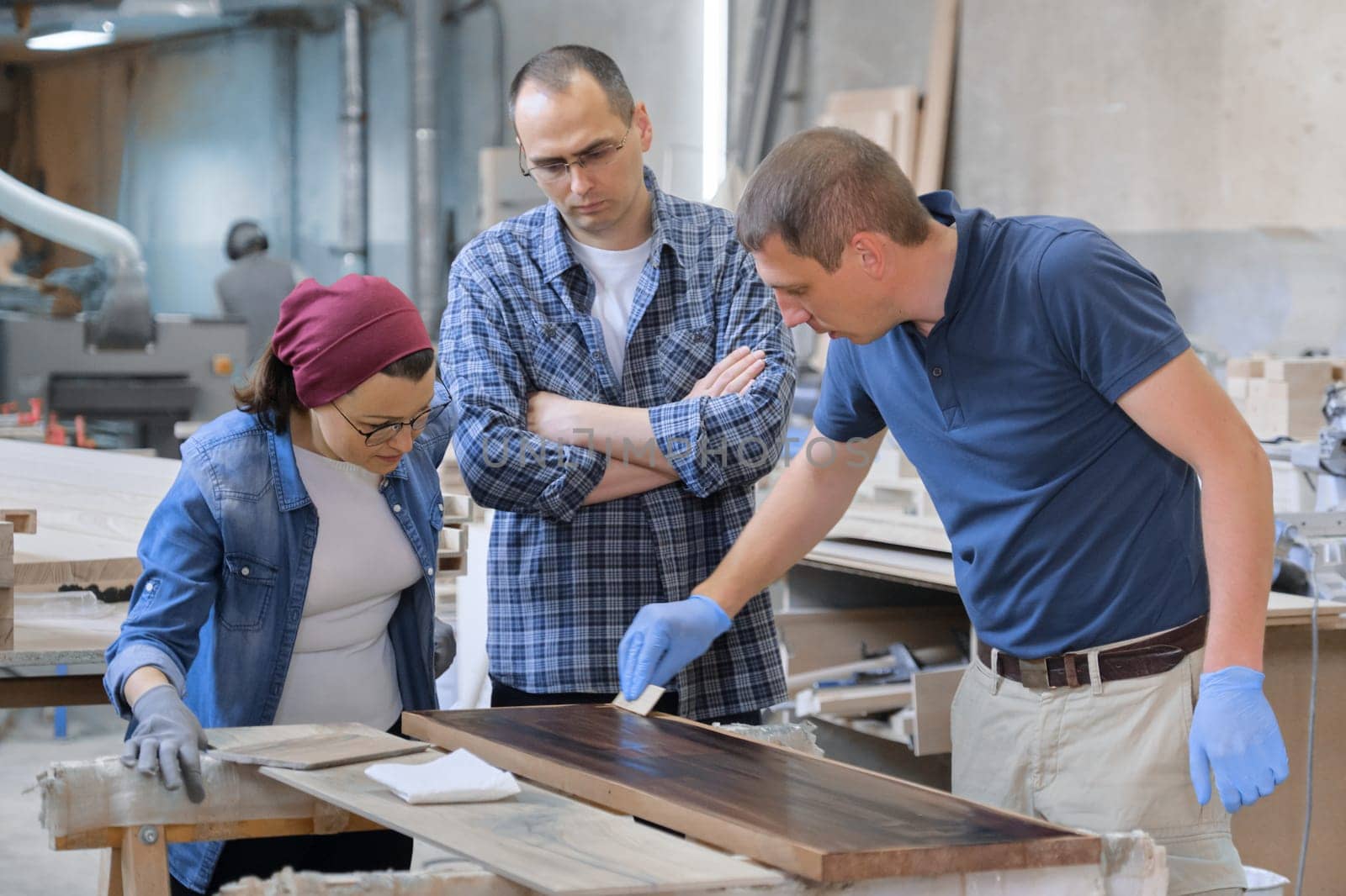 Workers in carpentry woodworking workshop, varnishing wooden plank with oil.